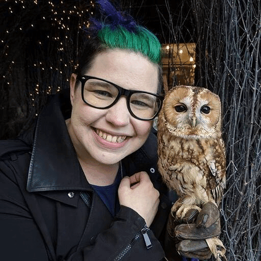 Andie Bardeck, Edmonton Screen’s Manager of Operations and Programming, smiling next to an owl perched on a glove with branches and lights in the background.